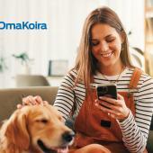 En kvinna sitter i soffan och tittar på mobiltelefonen och klappar en golden retriever