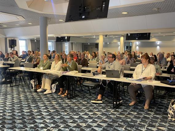 Konferenssiin osallistujat kuuntelemassa puhetta.
