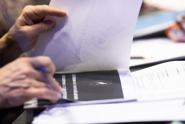Lähikuva käsistä, jotka selaavat Kennelliiton logolla varustettua paperipinoa kokouksessa
