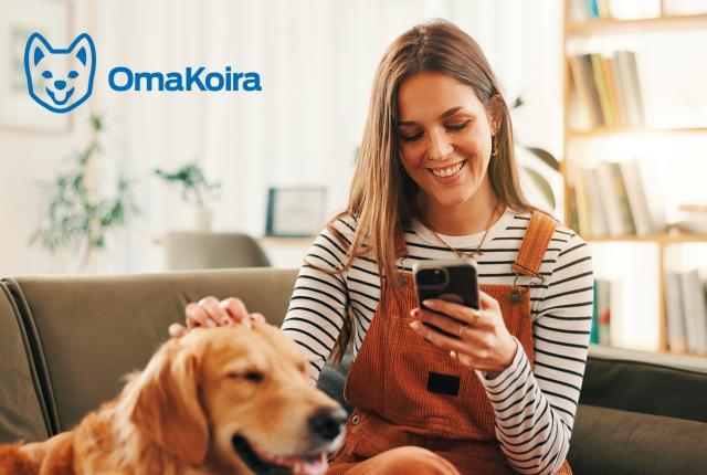 En kvinna sitter i soffan och tittar på mobiltelefonen och klappar en golden retriever