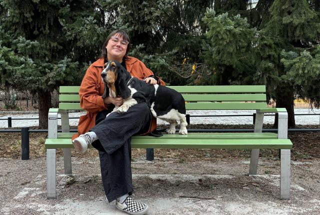Iida Mikkola istuu puiston penkillä basset hound -koiransa kanssa.