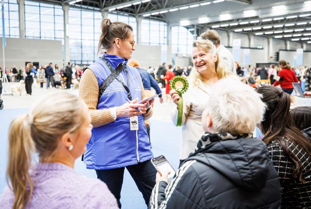 Koirien hyvinvointineuvoja antaa Kiva koirakko -palkinnon iloiselle koiranomistajalle Koiramessuilla.