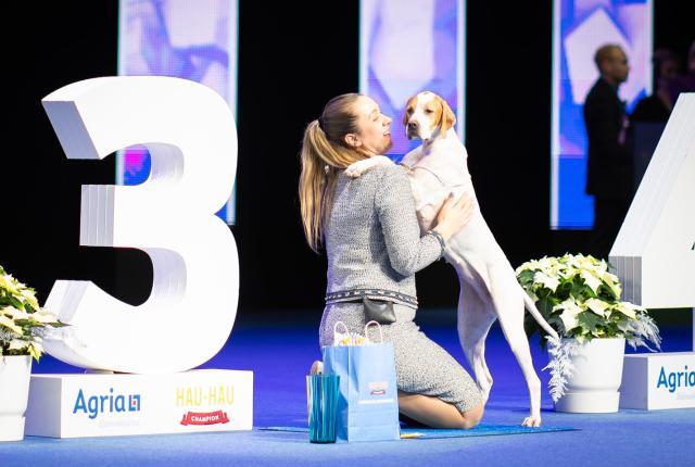 Ruskeavalkoinen pointteri ja nainen iloisina Koiramessujen palkintopodiumilla.