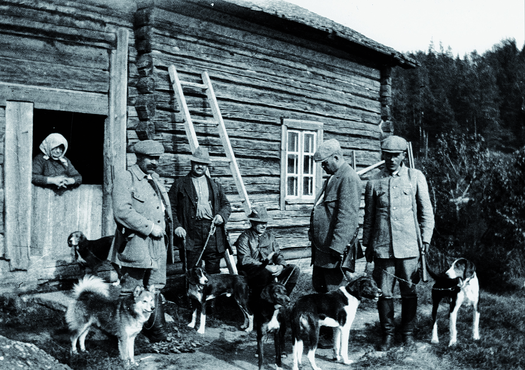 vanha mustavalkoinen kuva, jossa joukko miehiä ja ajokoiria seisoo hirsirakennuksen edessä